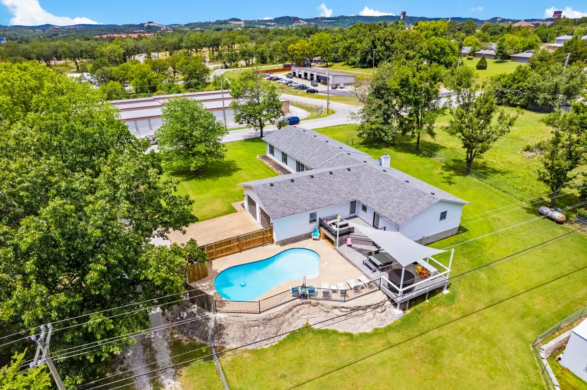 A broad exterior shot featuring the sparkling swimming pool, backyard patio with lounge chairs, lush green lawn, and surrounding trees. The scene exudes a joyful, sunny ambiance perfect for summer activities like swimming, sunbathing, family gatherings, or relaxing outdoors.