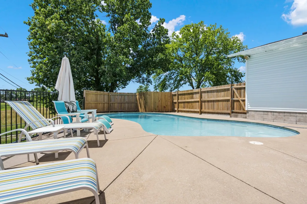An inviting scene of the swimming pool surrounded by lounge chairs, a secure fenced backyard, and lush trees creating a relaxed setting for outdoor enjoyment such as swimming, sunbathing, and family gatherings.