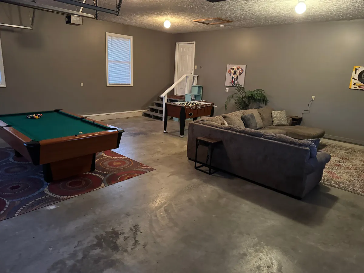 A close-up view of the game area, focusing on the pool table, foosball table, and a comfortable sofa. The arrangement suggests easy movement between games and a space that welcomes both active play and relaxed socializing.