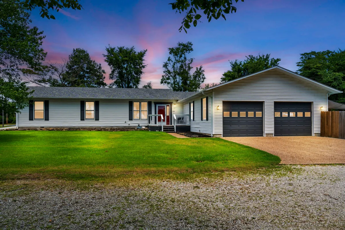 An inviting exterior shot of the front porch, two-car garage, and landscaped yard, showing plenty of space for arrivals and team gatherings. The relaxed, welcoming vibe suggests a comfortable home base for groups.