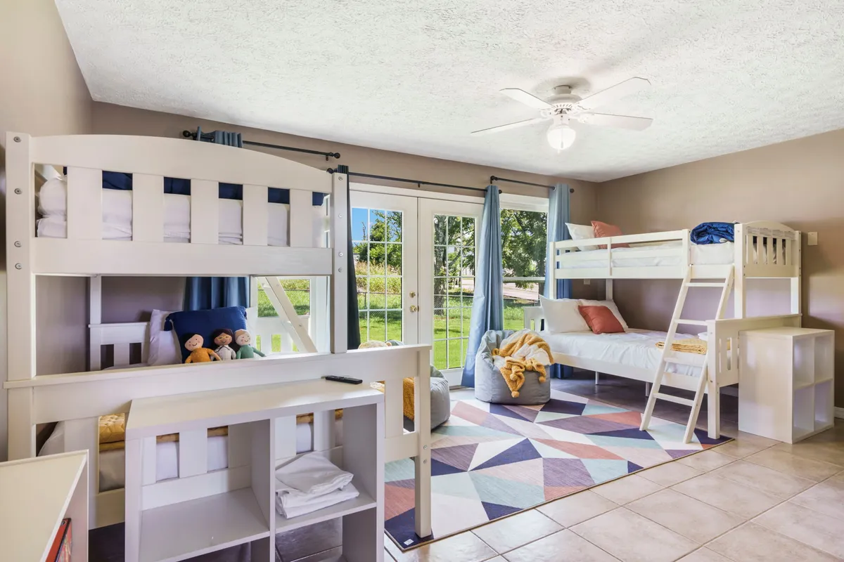 A playful interior image featuring bunk beds, a colorful area rug, and sliding glass doors that could lead to the yard or pool. The room is designed for shared, flexible sleeping arrangements and group fun, suitable for both kids and adults.