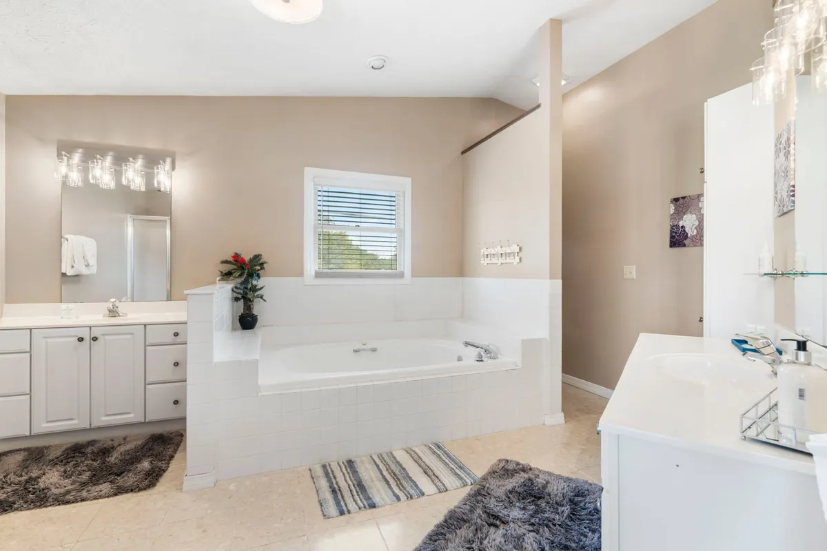 A spacious bathroom featuring a gleaming soaker tub, a mirrored vanity with a sink, and a window that bathes the room in natural light. The mood is tranquil, ideal for relaxing baths and peaceful morning routines.